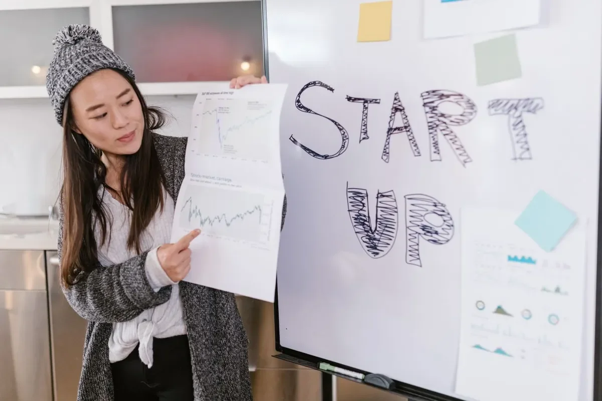 Una mujer presenta gráficos de crecimiento junto a una pizarra con las palabras start up escritas a mano