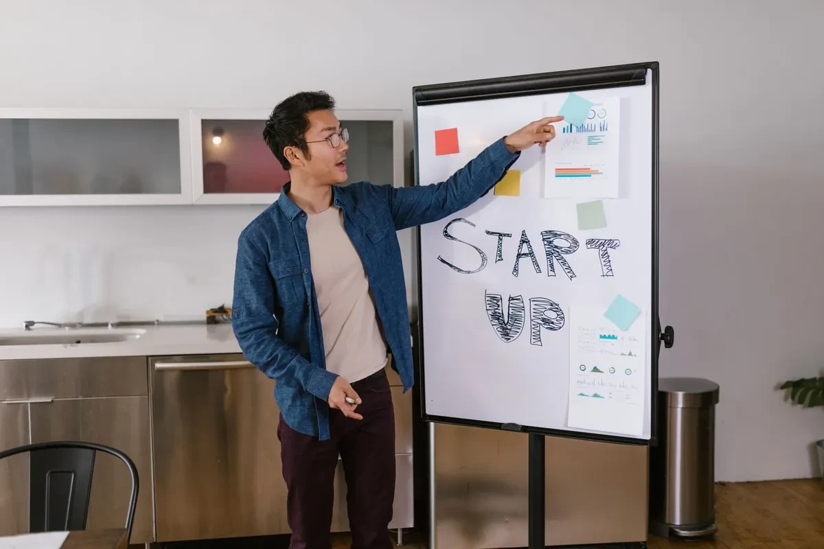 Un hombre presenta un proyecto señalando una pizarra con la palabra start up escrita a mano
