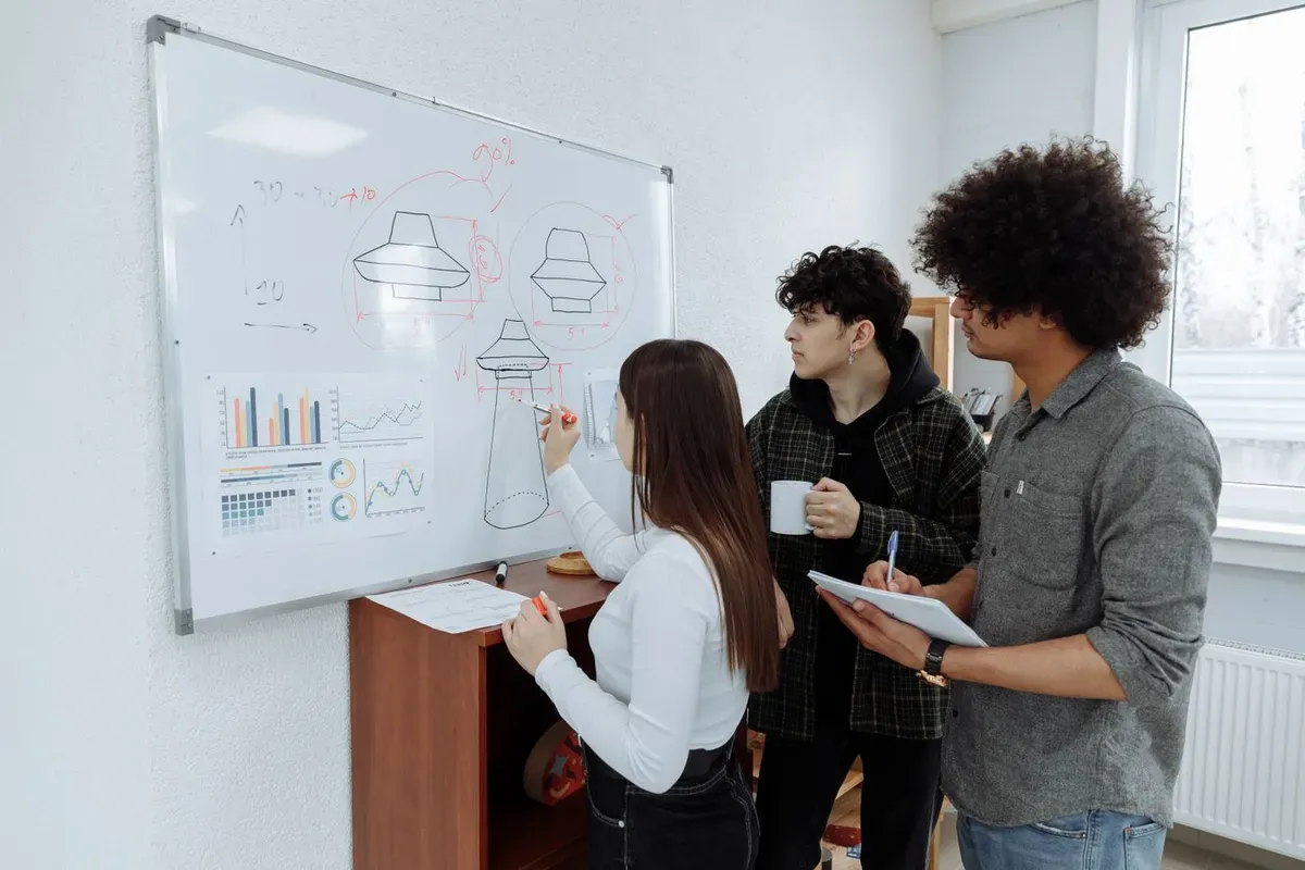 Tres jóvenes diseñan un producto dibujando bocetos y gráficos en una pizarra blanca
