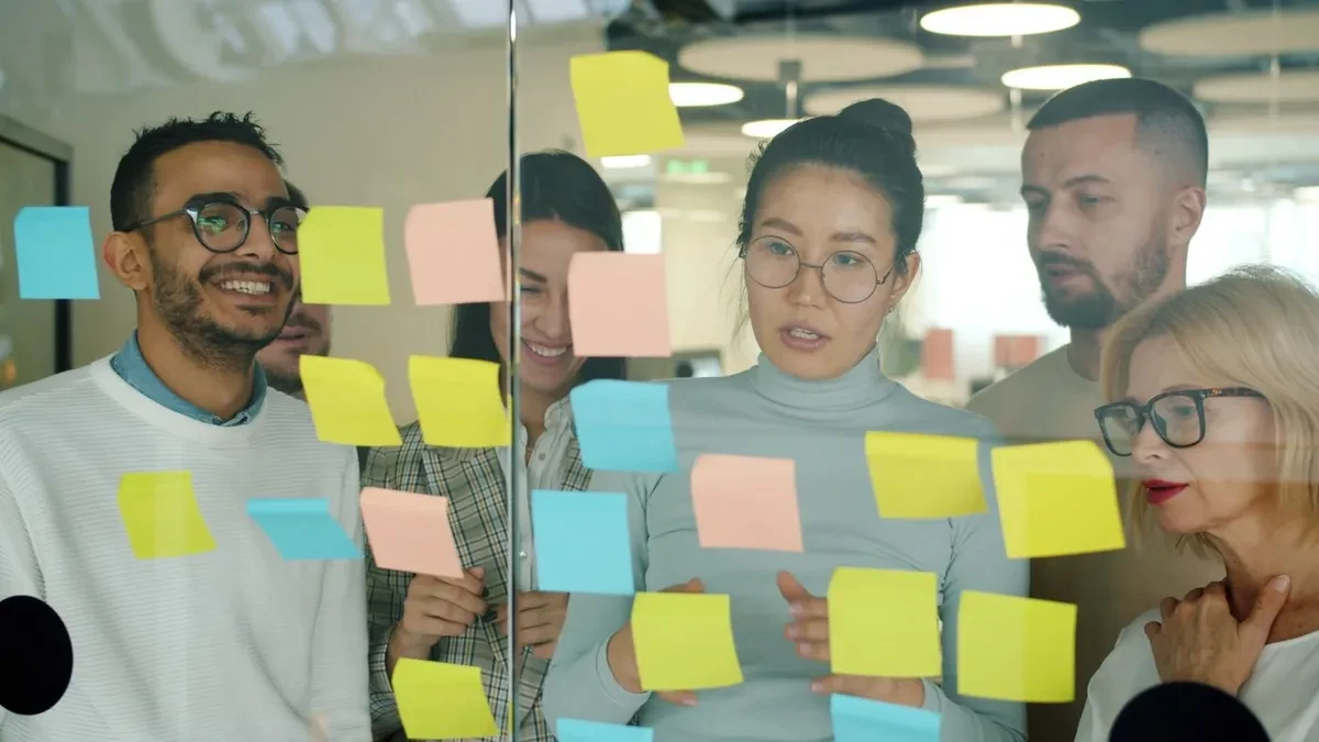 Un equipo de cinco personas revisa notas adhesivas de colores pegadas en una pared de cristal