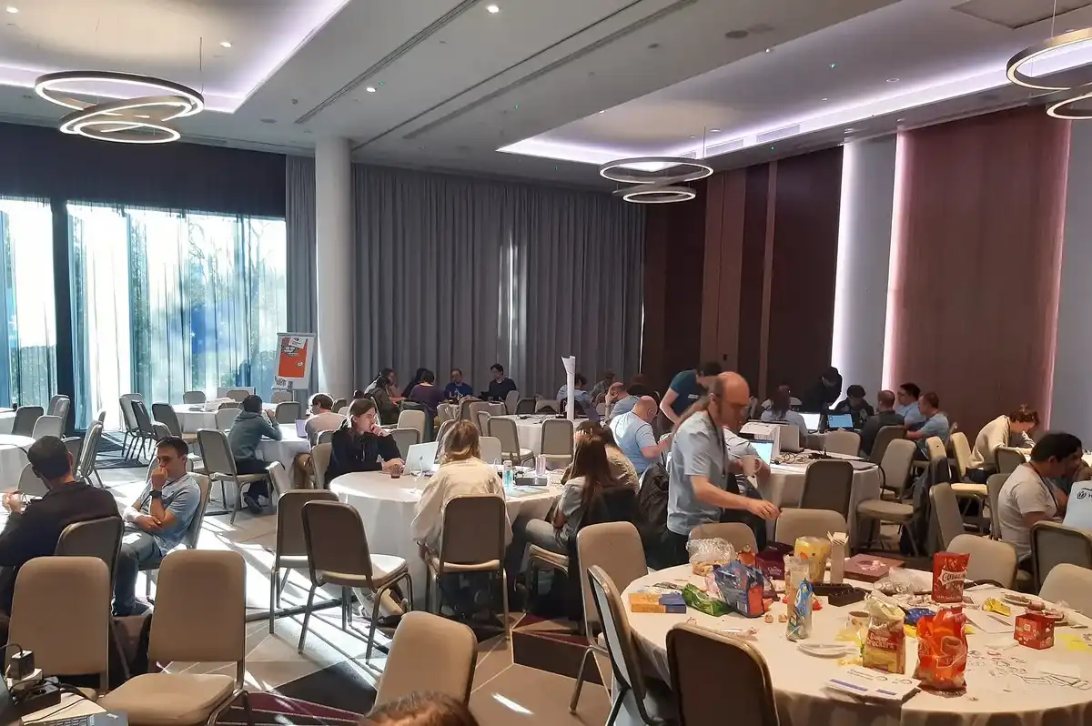 Decenas de participantes trabajan con portátiles en mesas redondas en la sala principal del Wikimedia Hackathon 2024 en Tallin